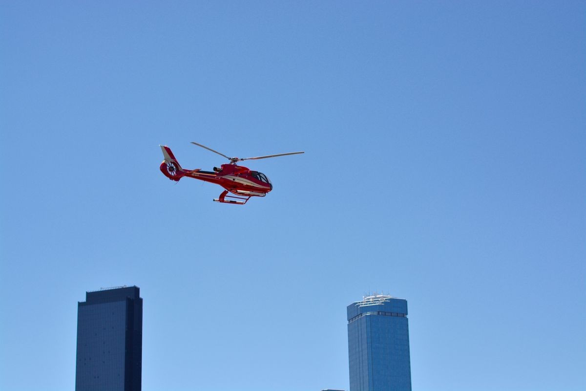 Helicopter, mid flight with skyscrapers on the background with clear light blue sky. 